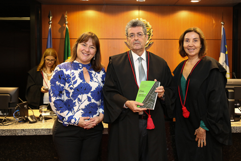 Fotografia do presidente do Tribunal segurando um livro e ladeado por duas autoridades. Todos vestem trajes formais e estão olhando para a câmera