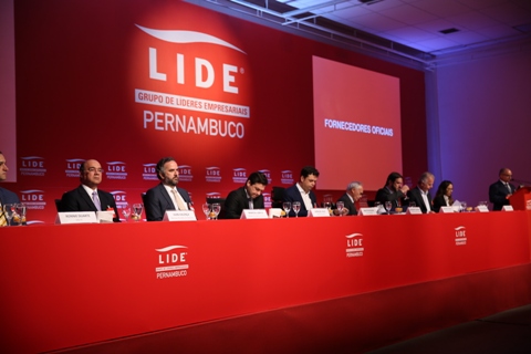 Fotografia de autoridades em uma mesa, atrás delas um painel vermelho com o texto &quot;LIDE, Grupo de Líderes Empresariais Pernambuco&quot; 