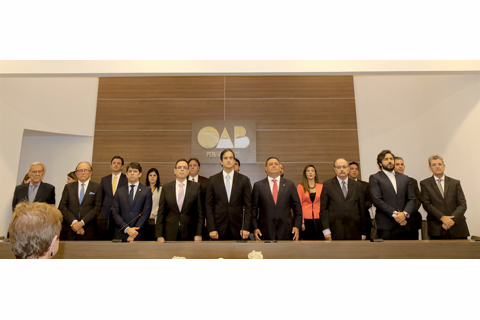 Grupo de pessoas com vestimentas formais, em pé, em cima de um palco