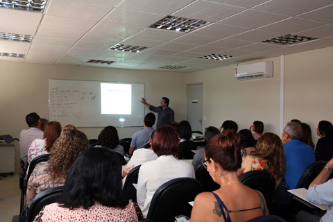 Foto de uma sala de aula, com professor ao quadro e alunos sentados