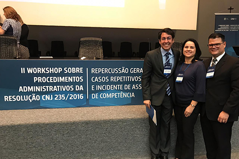 Fotografia de três pessoas em pé, próximas a um banner escrito "II Workshop sobre procedimentos administrativos da Resolução CNJ 235/2016 - Repercussão Geral, Casos Repetitivos e Incidentes de de assunção de competência