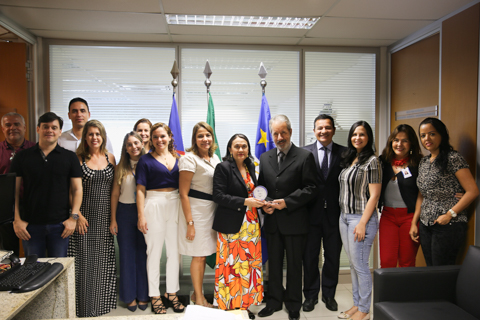 Fotografia de 14 pessoas em pé, olhando para câmera. Ao fundo as bandeiras do Brasil, Pernambuco e Recife