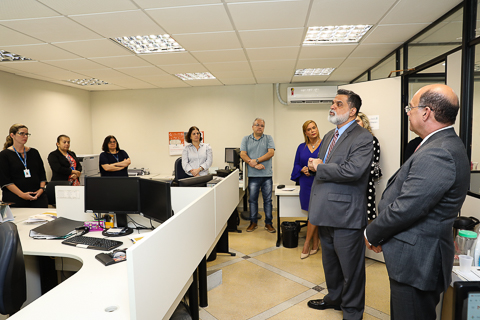Equipe da EJ, em pé, na sala, escuta pronunciamento do ministro