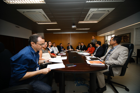 Fotografia de pessoas sentadas em volta de uma mesa de reuniões, lendo relatórios