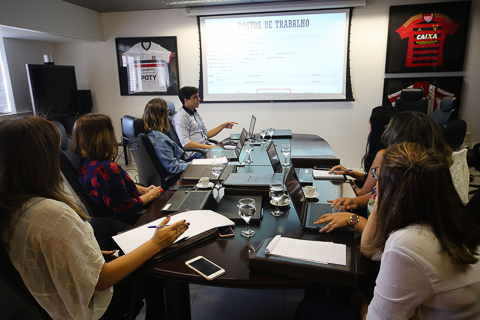 Fotografia de pessoas sentadas a mesa de reuniões, olhando para apresentação em power point