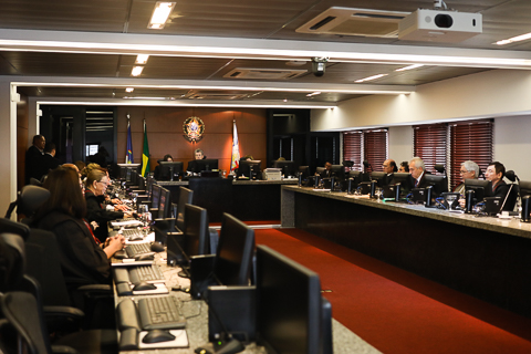  Mesa em &quot;U&quot; com desembargadores setados em volta dela, todos usam toga e têm um computador.