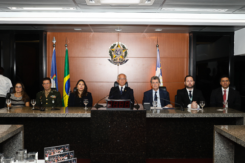 Fotografia de sete autoridades sentadas em uma mesa. Atrás delas estão o Brasão da República e as Bandeiras do Brasil e Pernambuco 