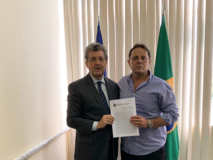 Fotografia de duas autoridades segurando um papel. Atrás delas, estão dispostas bandeiras do Brasil e Pernambuco