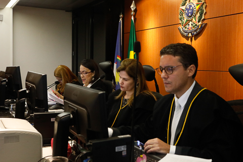 Fotografia de quatro pessoas, usando toga, sentadas à frente de computadores