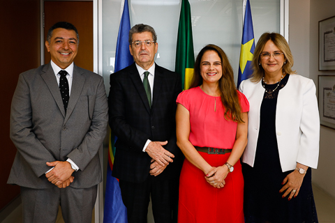 Fotografia de quatro autoridades posando para câmera. Atrás delas, as bandeiras do Brasil, Pernambuco e Recife