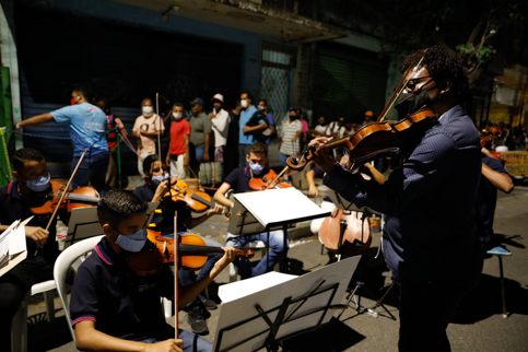 Foto da Orquestrado Alto da Mina tocando enquanto pessoas em situação de rua se organizam em fila para receberem doações