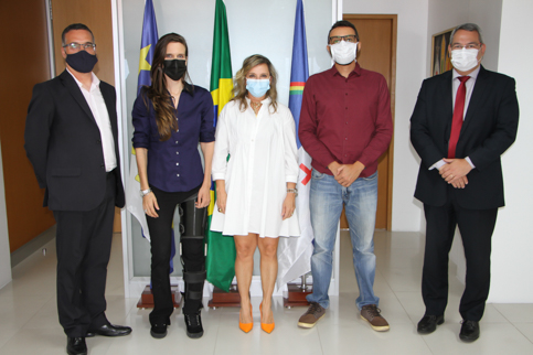 Retrato de cinco pessoas em trajes profissionais. Elas posam junto a bandeiras do Brasil, Pernambuco e Recife