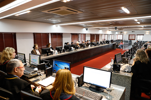 Fotografia dos desembargadores reunidos na sala do Pleno. Eles usam toga e trabalham com computadores