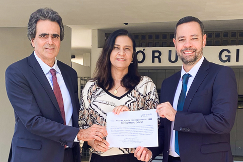 Foto do corregedor, do juiz e da diretora segurando um certificado 