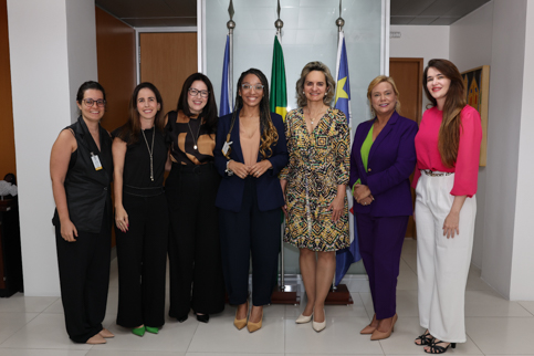 fotografia de seis mulheres, em roupas profissionais, em pé, olhando para a câmera