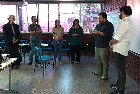 Fotografia de um rapaz apresentando um trabalho e outras cinco pessoas assistindo