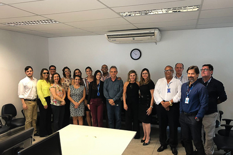 Fotografia de 17 pessoas, em pé, olhando para a câmera, dentro de uma sala de trabalho