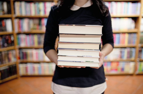 Foto em super close mostrando uma mulher segurando uma pilha de livros