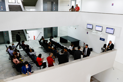 foto do alto mostrando sala de recepção com pessoas sentadas em longarinas