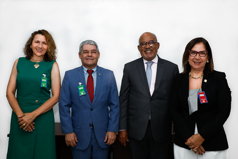 retrato de quatro pessoas, com trajes profissionais, em pé, olhando para a câmera