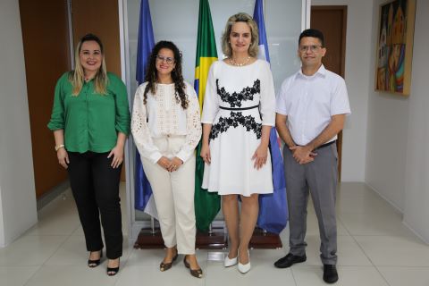 Foto da presidente Nise Pedroso junto com o novo empossado e as duas novas empossadas. Todos usam trajes profissionais e estão em pé, em uma sala de reuniões