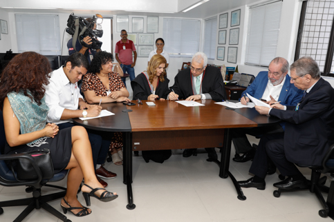 fotos de sete pessoas assinando documentos em uma mesa