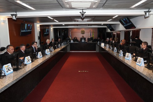 Foto mostra a sala do Pleno, com 17 pessoas adultas sentadas atrás de monitores de computador