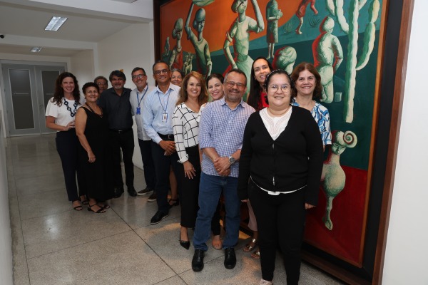Grupo de servidores posa em corredor institucional, ao lado de grande painel artístico colorido.