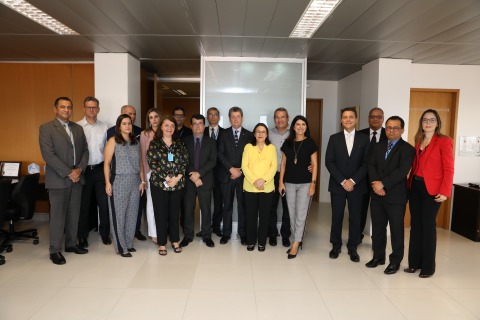 Fotografia de várias pessoas, em pé, olhando para a câmera. Estão dentro de uma sala de reuniões, próximo a bandeiras do Brasil, Pernambuco e Recife