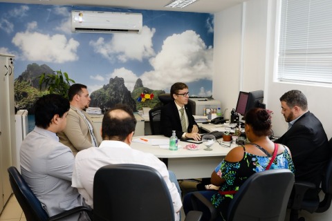 Fotografia de pessoas sentadas à mesa de reunião. Elas usam trajes profissionais