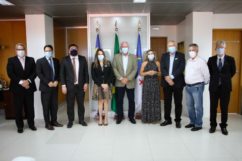 Autoridades posando para foto, junto a bandeiras e dentro de uma sala de reuniões