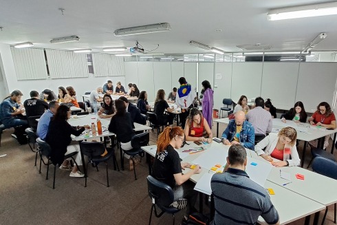 fotografia de uma sala ampla, com pessoas trabalhando em seis diferentes mesas