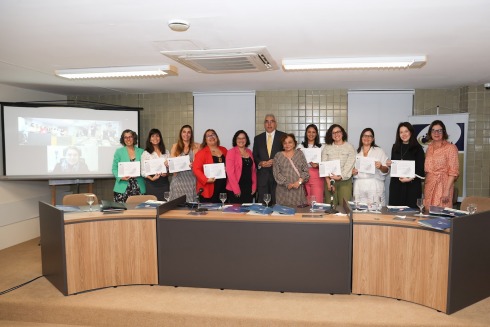 fotografia de várias mulheres segurando um certificado. Elas estão no palco de um auditório. No grupo, há um homem. Todos usam roupas formais