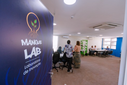 Foto mostra a porta da sala do manguelab aberta e, dentro dela, pessoas conversando