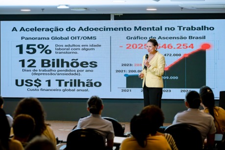 Na foto, uma senhora apresenta palestra, diante de uma plateia