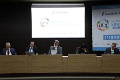 autoridades em mesa de eventos. Atrás deles há um telão que mostra apresentação sobre a COP30