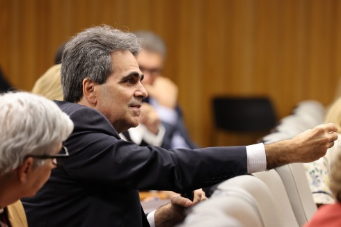 Foto mostra um homem grisalho sentado, usando terno e falando