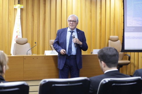 Foto mostra um homem de cabelos brancos em pé, vestindo terno azul e segurando um microfone