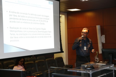 Fotografia de Luiz Eduardo explicando conteúdo de um slide reproduzido em um telão próximo