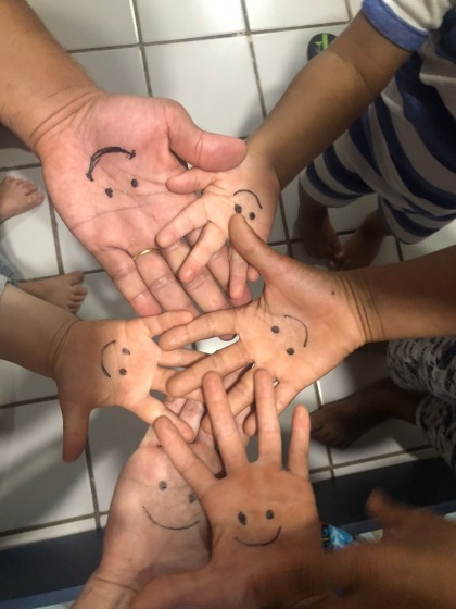 Foto das mãos da família unidas com as palmas para cima. Em cada uma tem um rostinho sorrindo desenhado.