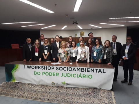 Fotografia de várias pessoas reunidas atrás de um banner com os dizeres &quot;1º Workshop Socioambiental do Poder Judiciário&quot;