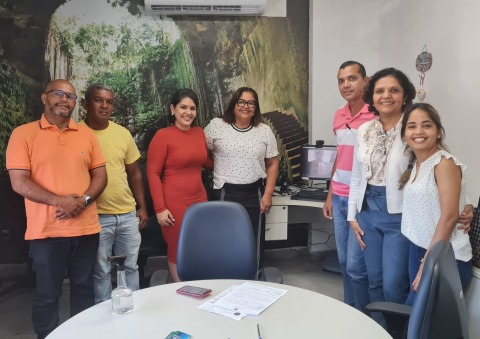 foto de pessoas dentro de uma sala de reuniões. A parede está adesivada com uma imagem de natureza