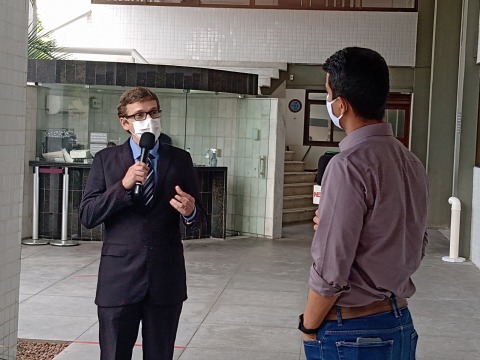 Fotografia do juiz Eduardo Câmara participando de entrevista. Tanto ele como o jornalista usam máscara e falam ao microfone