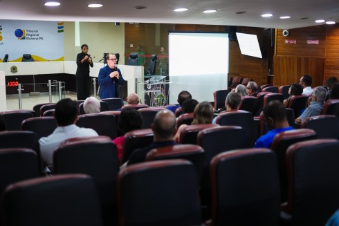 Foto mostra um auditório com um professor em pé, enquanto alunos sentados assistem