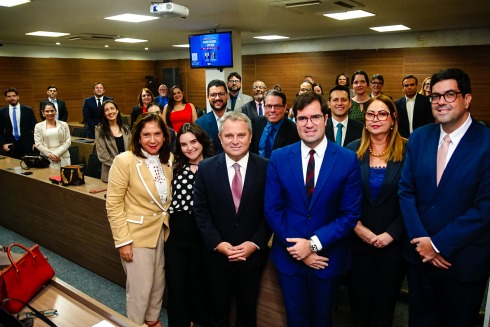 Foto mostra cerca de 40 pessoas em pé, em um auditório