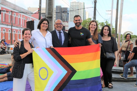 Fotografia de seis pessoas posando com a bandeira da comunidade LGBTQIA+