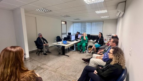 Fotografia onde aparecem adultos sentados, reunidos numa sala de audiência