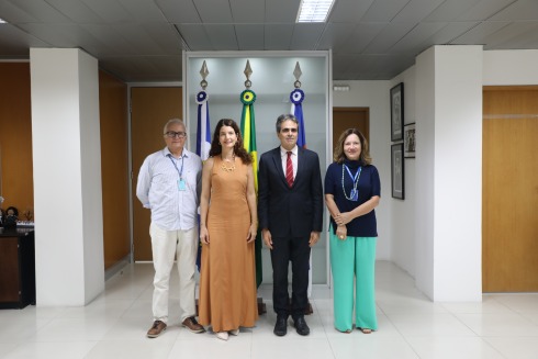 Quatro pessoas posam em frente às bandeiras de Pernambuco, do Brasil e do Recife