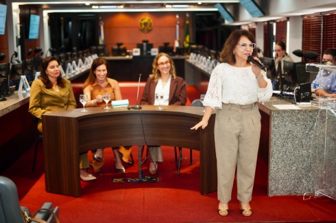 Foto mostra três mulheres sentadas em uma mesa e uma em pé, falando