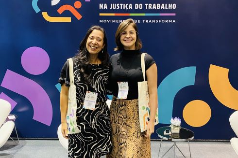 foto duas mulheres posando segurando sacolas ao fundo painel do evento